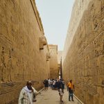 Visitors walk through a corridor of an ancient Egyptian temple with hieroglyphic carvings.